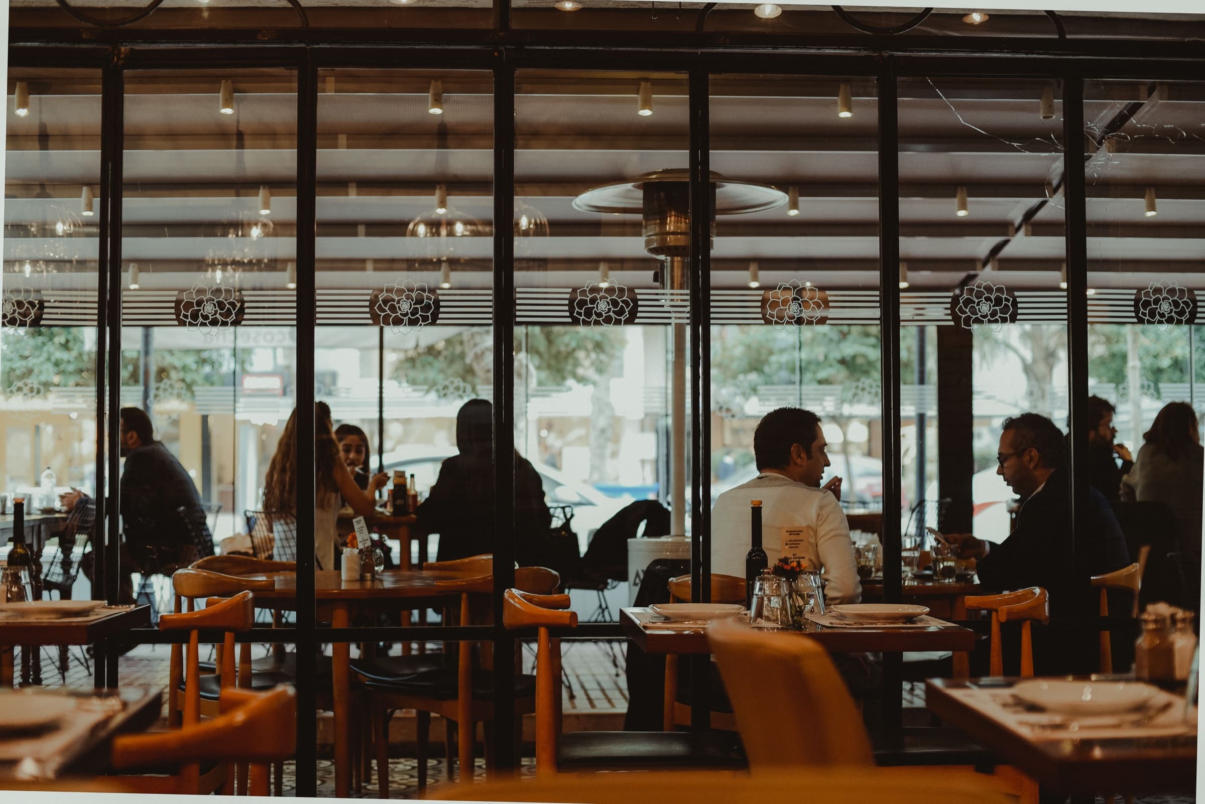 Guests dining at tables inside a warmly lit restaurant with glass partitions and wooden chairs